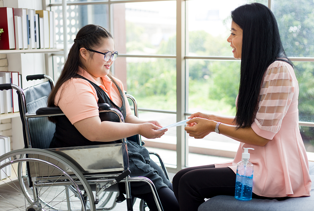 Girl in wheel chair smiling with psychologist in light bright room