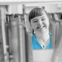 Girl with ID chooses a book on a shelf in the library. Education for disabled children