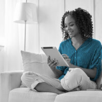 Happy teen girl holding pad computer gadget using digital tablet technology sitting on couch at home. Smiling young woman using apps
