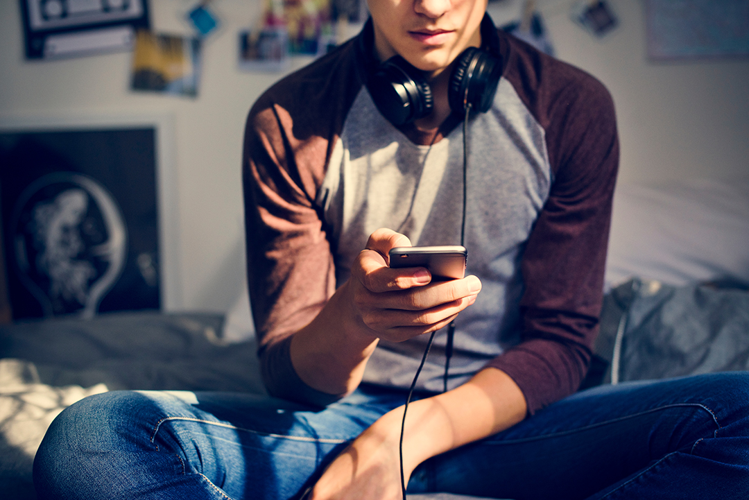 Teenage boy in a bedroom listening to music through his smartphone