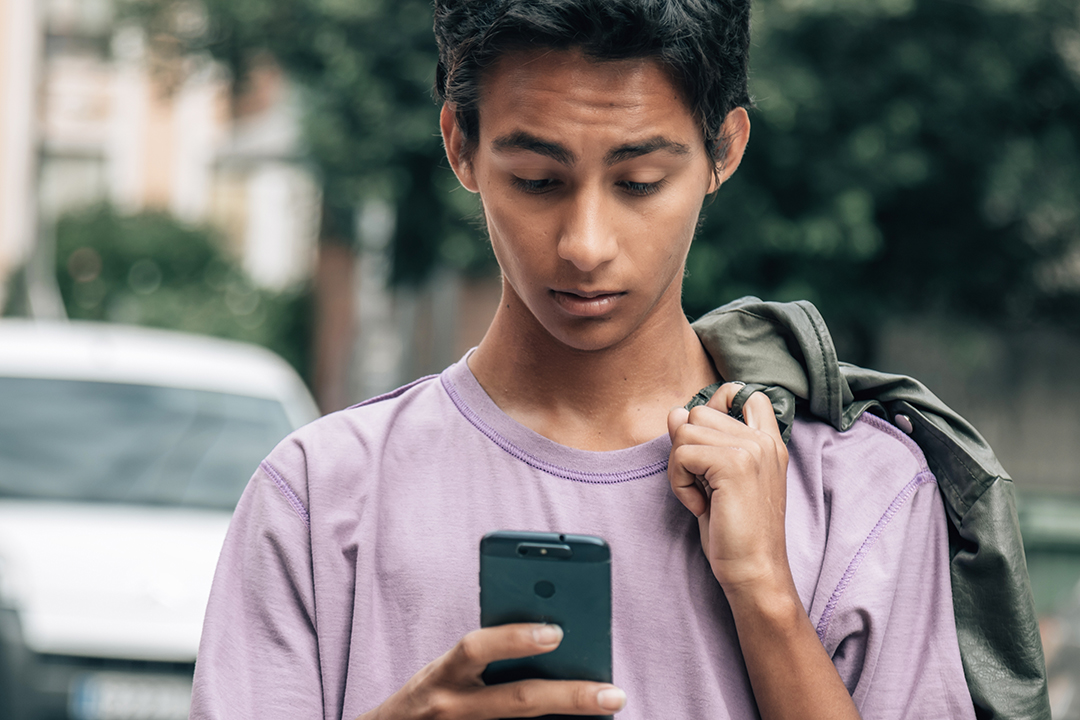 Teenage boy looking at the phone with disgusted or angry gesture on the street