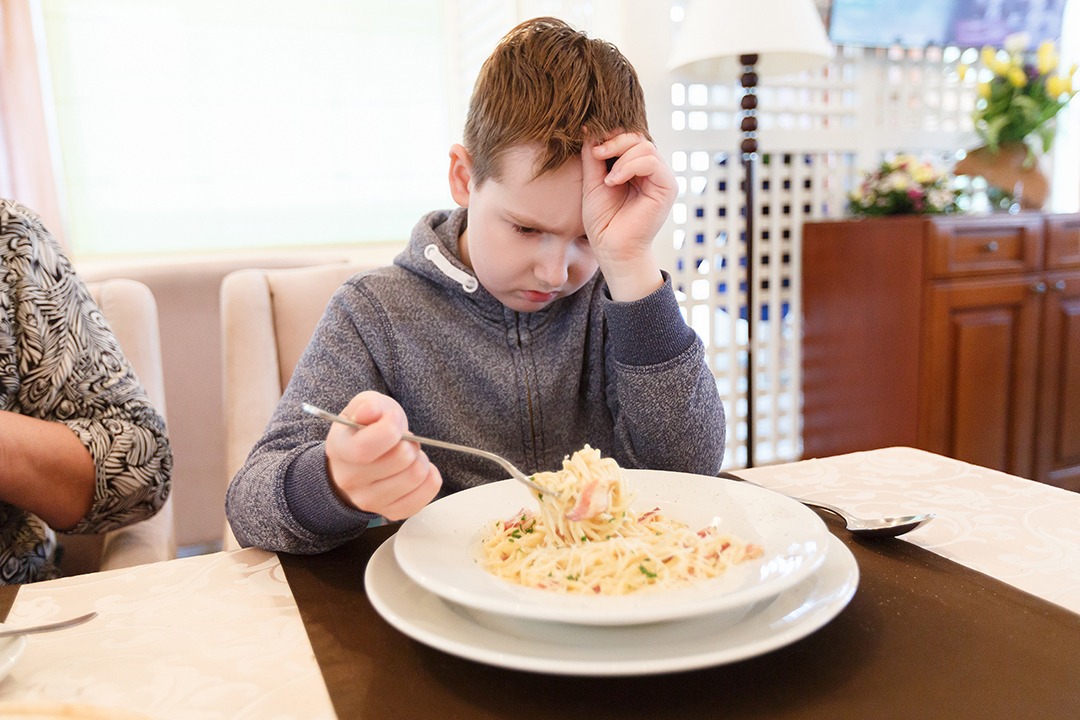 Preteen handsome boy with a plate of pasta refuse to eat disgust grimace