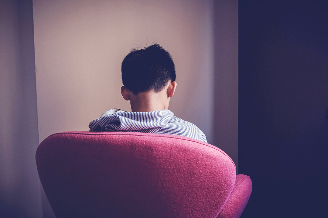 Sad preteen boy sitting alone in chair facing wall, depressed,introvert, autism awareness, children mental health,psychology teen autism spectrum disorder, social distancing, self isolation concept