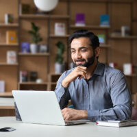 Smiling indian professor working on laptop in to review acamenic papers