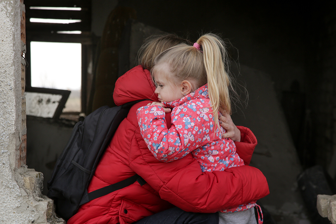 Female volunteer with mobile gadgets communicating to one of refugees while sitting on squats in front of her in shelter for migrants