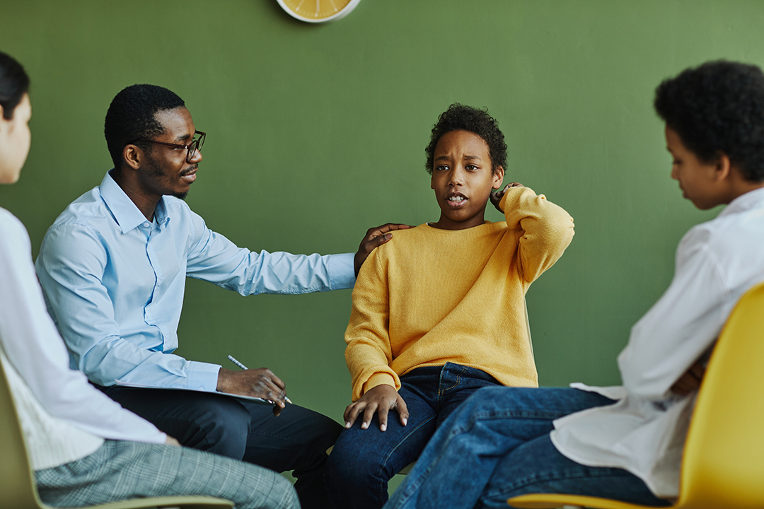 Dissatisfied schoolboy touching back of head while describing his problem at session and school psychologist supporting him