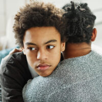 Portrait of son hugging his father, together at home. Son caring for his father, putting hand on his shoulder, comforting and consoling him. Family love, bonding, care and confidence