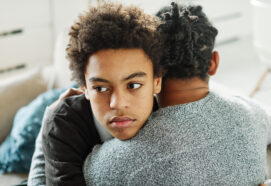 Portrait of son hugging his father, together at home. Son caring for his father, putting hand on his shoulder, comforting and consoling him. Family love, bonding, care and confidence