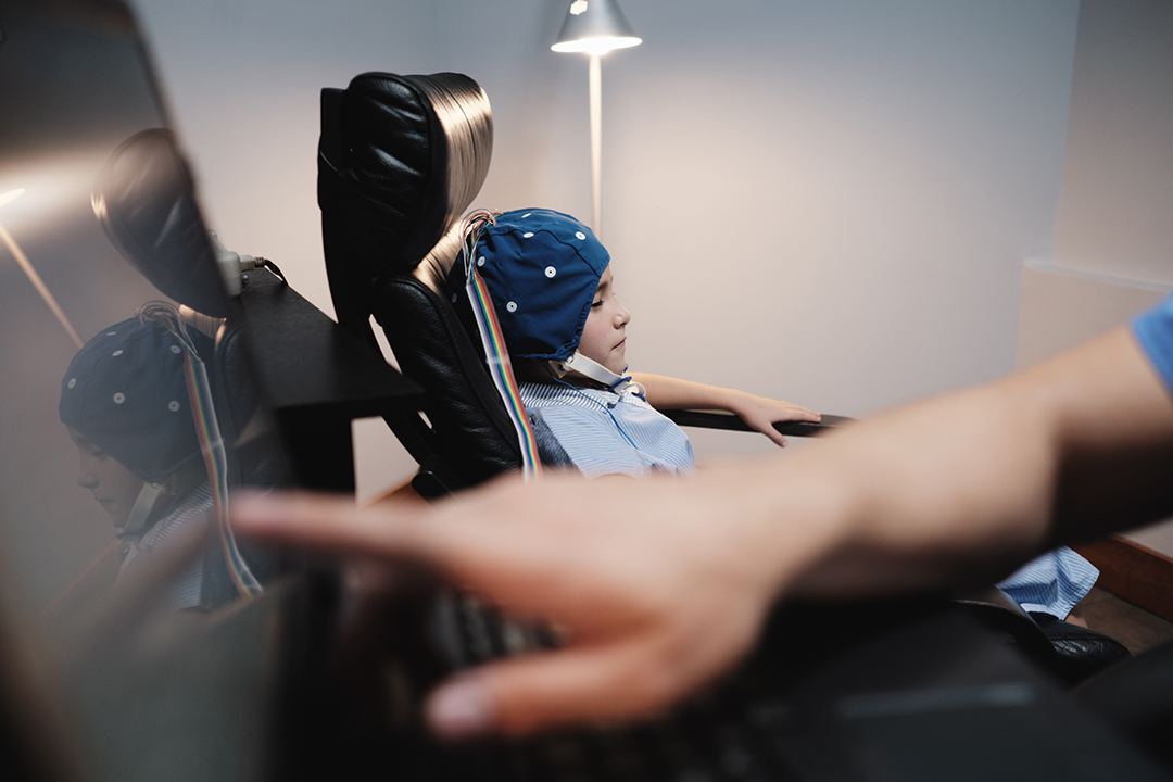 A young pediatrician doctor reads little girl electroencephalogram results on the computer screen. Brain waves on monitor representing the patients EEG results and neurological health. Pediatrics