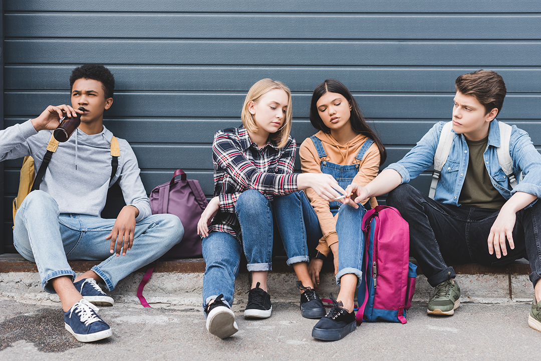 teenagers sitting, drinking beer from glass bottle and holding cigarette