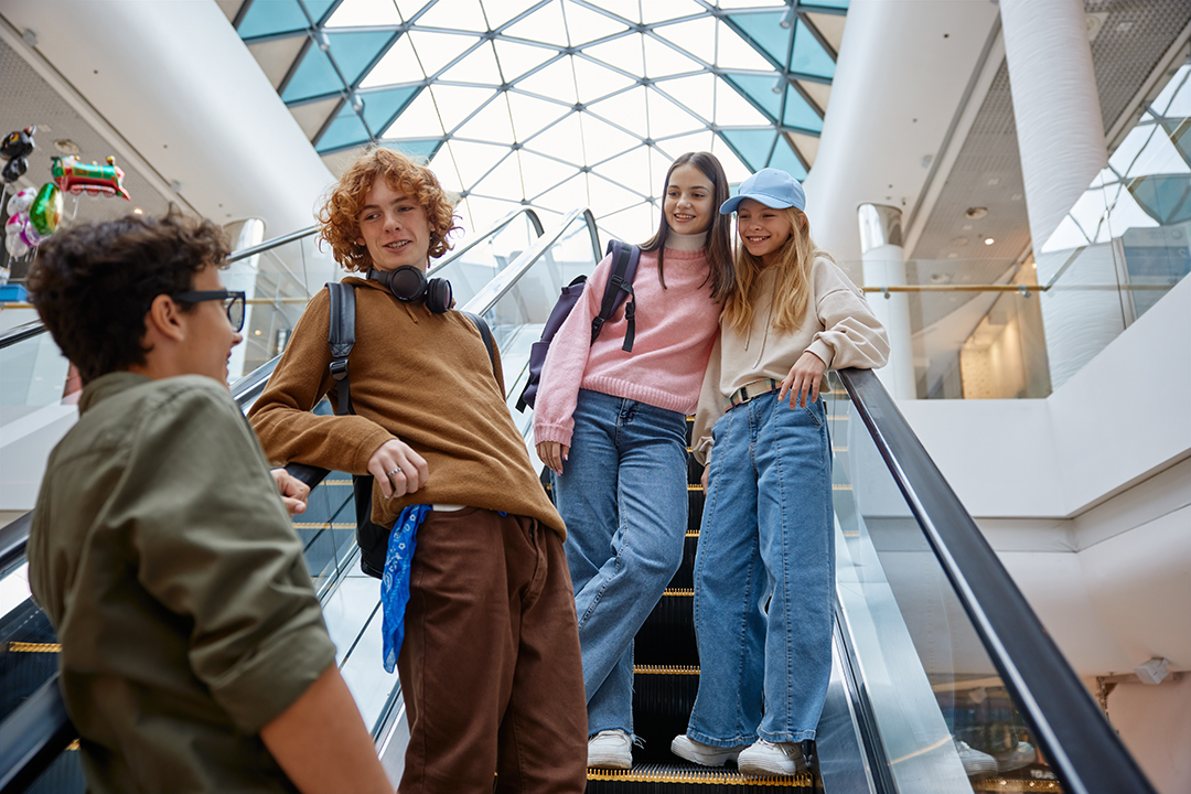 Happy teenage friends team moving staircase at shopping mall