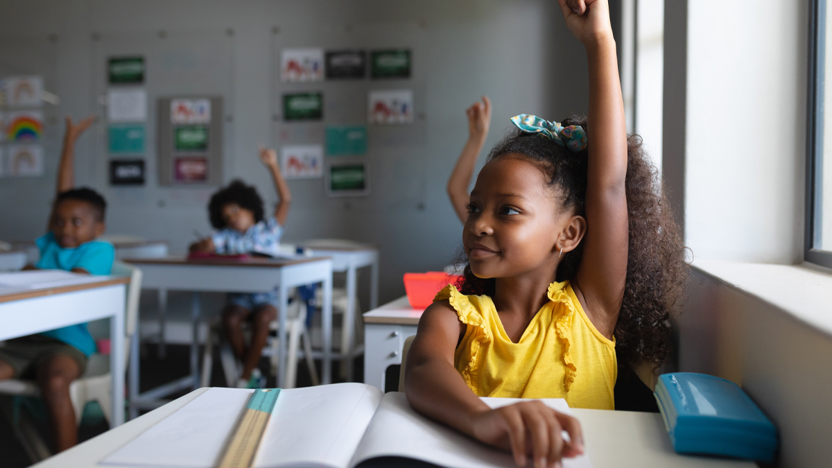 African american elementary school students with hands raised sitting at desk in classroom. unaltered, education, childhood, learning and school concept.