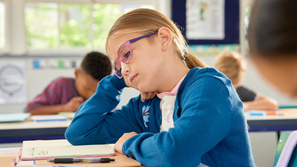 Bored schoolgirl tired of learning and doing homework while trying not to fall asleep, attention deficit, lack of concentration and distraction concept. Little girl wearing spectacles feeling bored.