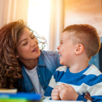 Kind mother helping her son doing homework in kitchen. Children's creativity. Portrait of smiling mother helping son with homework in kitchen at home