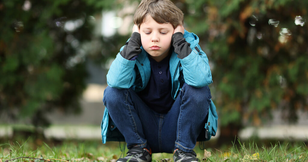 Autism concept. Lonely little boy covering his ears outdoors