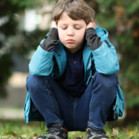 Autism concept. Lonely little boy covering his ears outdoors