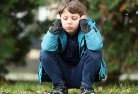 Autism concept. Lonely little boy covering his ears outdoors