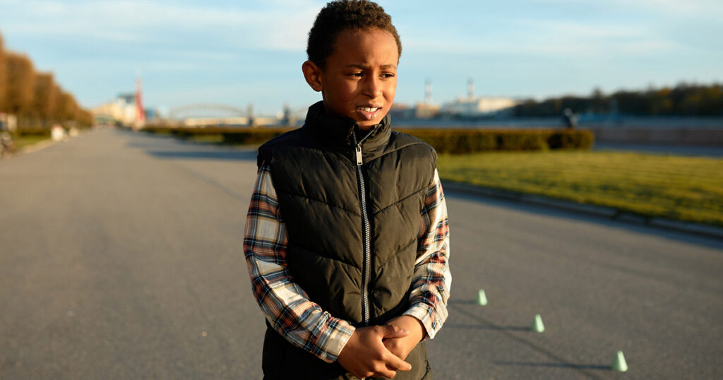 Upset worried black boy kid standing on background with city park holding his stomach with painful facial expression and miserable look, feeling pain in belly after training outdoor