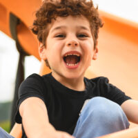 child smiling whilst holding onto a slide in a park
