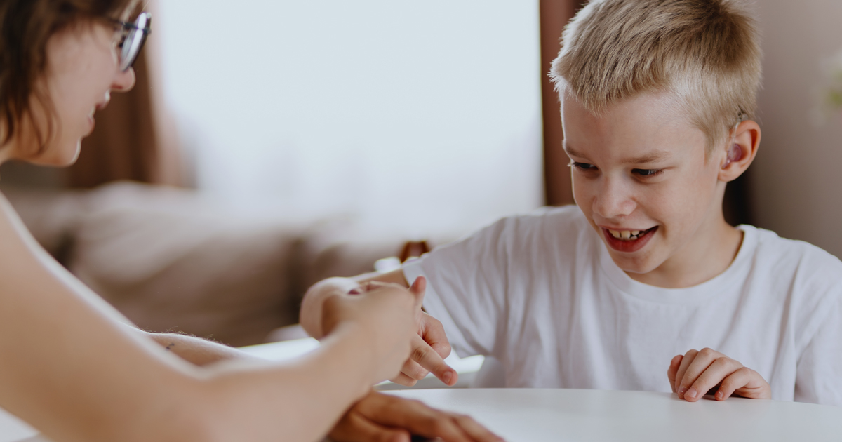 Young mother helps her hard-of-hearing son with schoolwork at home. A natural, heartfelt moment of inclusion, care, and rehabilitation, highlighting love, support, and everyday learning