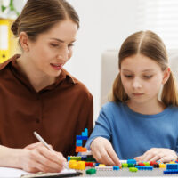 Girl playing with toys at white table during consultation with professional child psychologist indoors