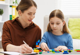 Girl playing with toys at white table during consultation with professional child psychologist indoors