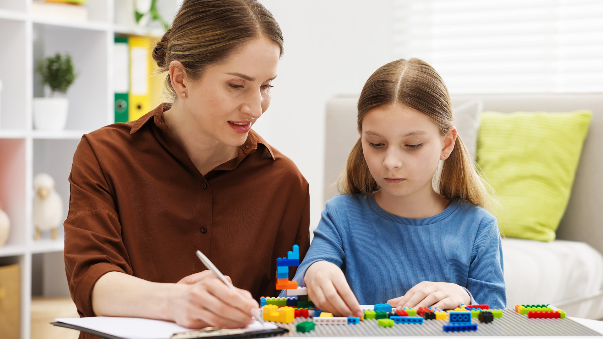 Girl playing with toys at white table during consultation with professional child psychologist indoors