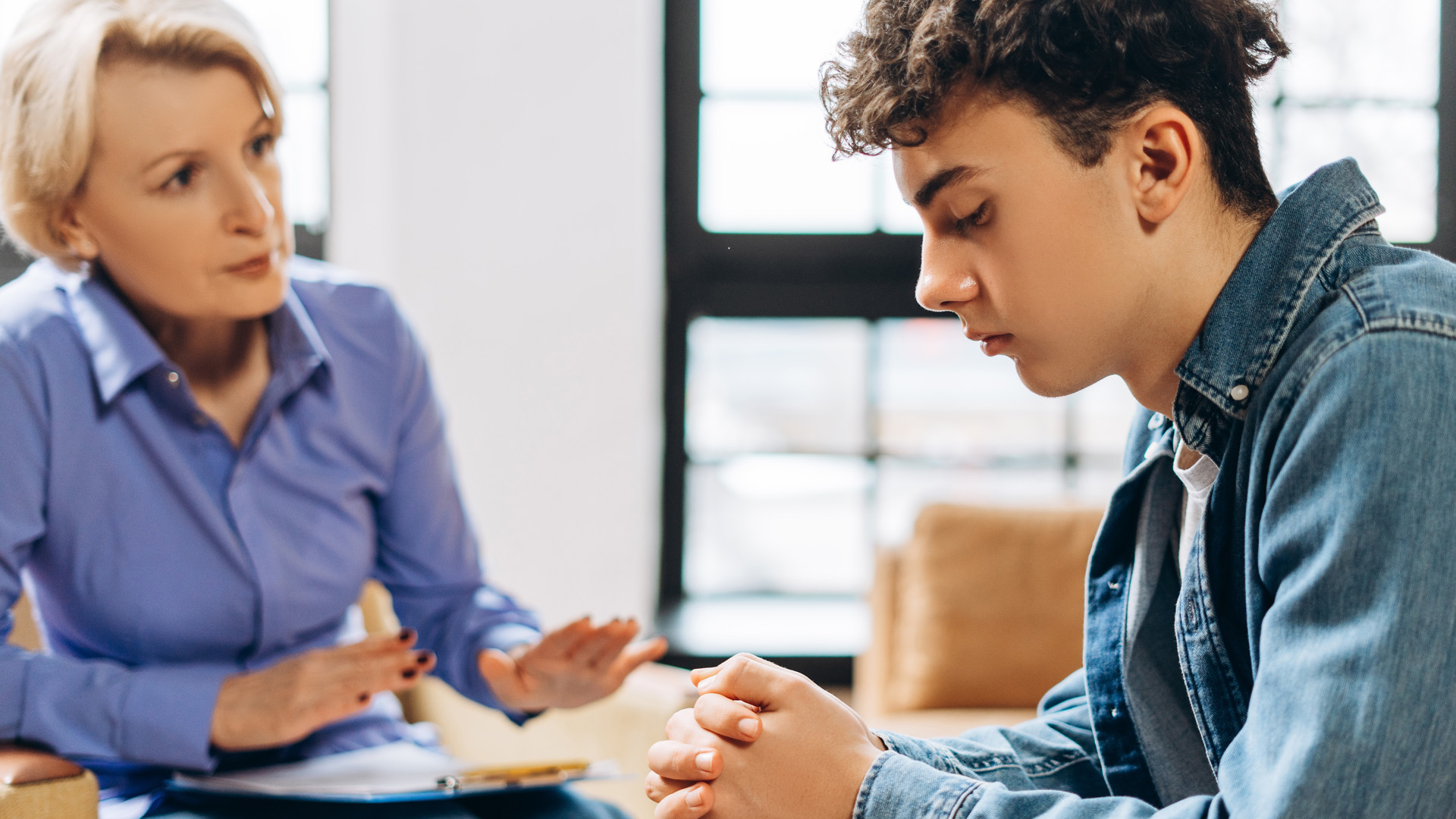 Portrait of professional female psychologist working with teenager boy in office while explaining. 