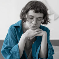 Sad upset teenage girl sitting on sofa, looking down with withdrawn expression, resting chin on hands. Teen uncertainty, social isolation, low self confidence, introversion and emotional discomfort.