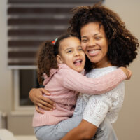 Portrait of happy mother and daughter hugging each other in bedroom at home