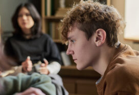 Teenager boy sitting in profile listening attentively within a group with multiethnic young people and teenagers in background participating in discussion