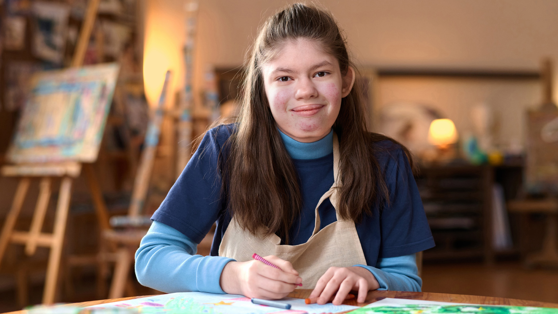 Front view portrait of young girl with Williams syndrome smiling at camera sitting at table in art studio Front view portrait of young girl with Williams syndrome smiling at camera sitting at table in art studio