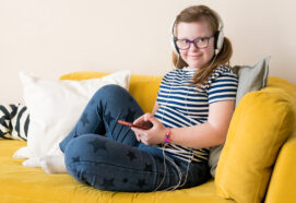 Portrait of Teenage girl with Down syndrome listening to music in headphones sitting on sofa at home