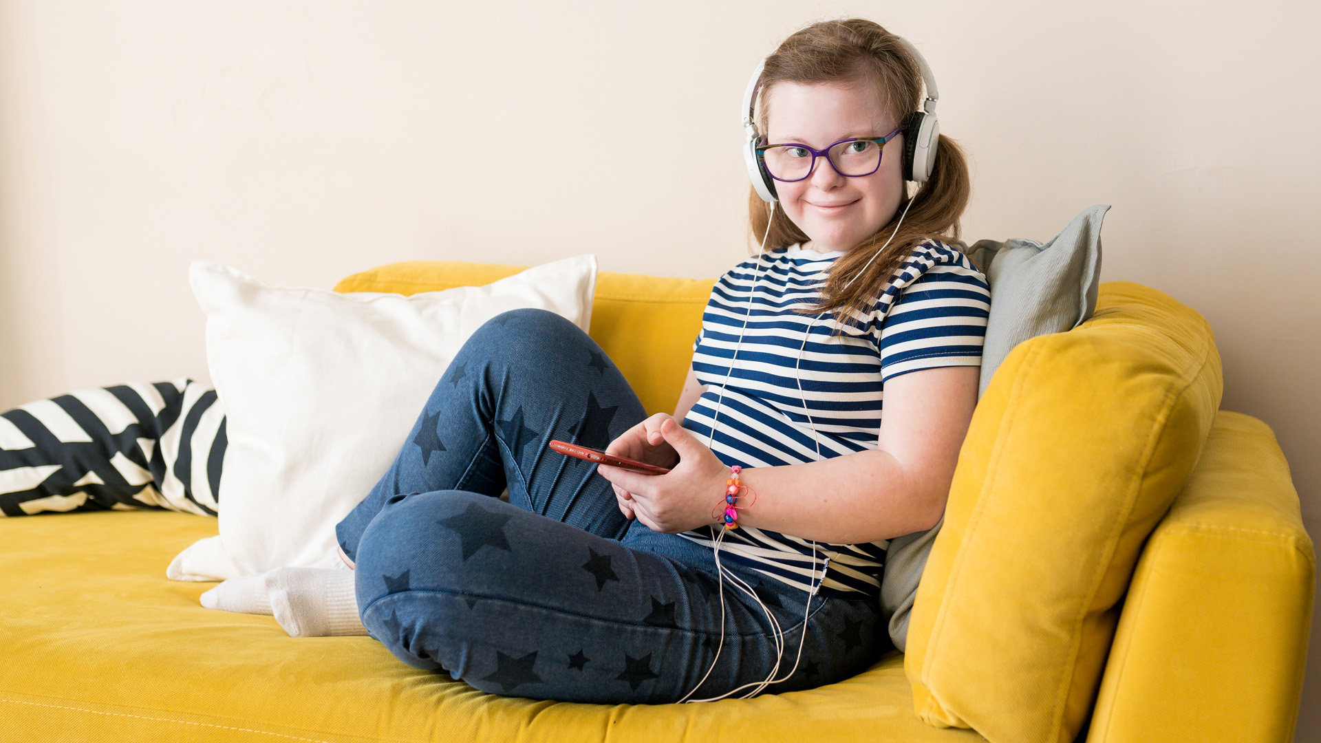Portrait of Teenage girl with Down syndrome listening to music in headphones sitting on sofa at home Portrait of Teenage girl with Down syndrome listening to music in headphones sitting on sofa at home