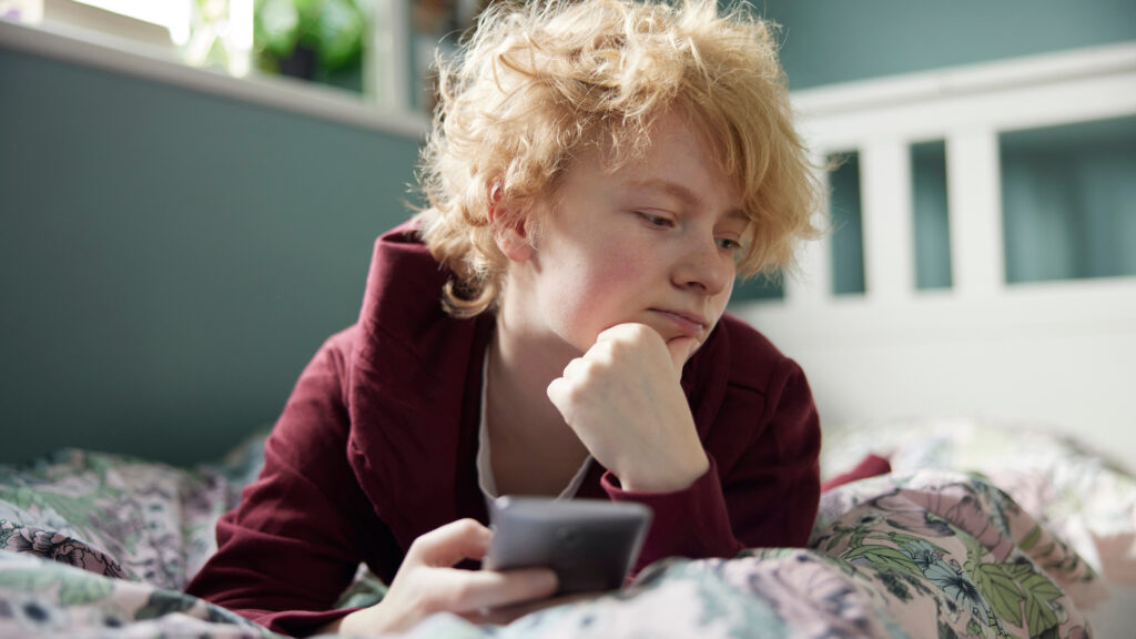 Unhappy Teenage Girl Lying On Bed At Home With Mobile Phone Unhappy Teenage Girl Lying On Bed At Home With Mobile Phone